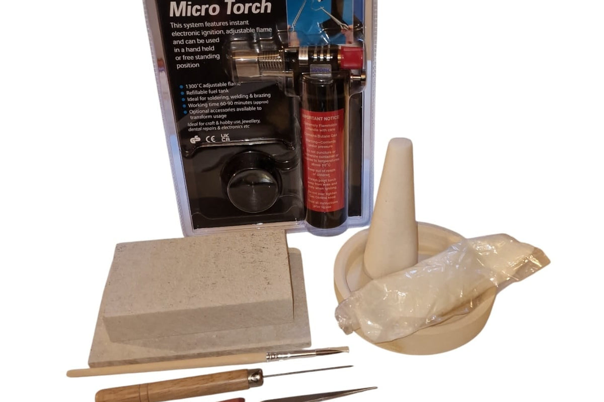 A collection of soldering tools including a butane soldering torch, soldering mat, soldering block, paintbrush, borax cone and tray, safety pickle, tweezers, and a solder probe.