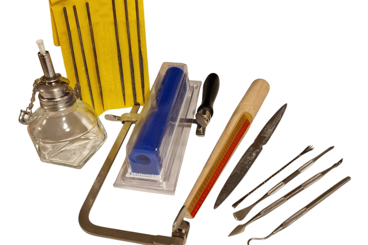 A collection of wax carving tools including a saw frame, wax files, a wax needle, a wax stick with blade, and a spirit lamp wax container.