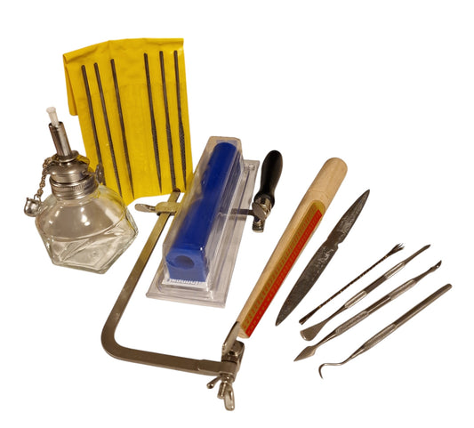 A collection of wax carving tools including a saw frame, wax files, a wax needle, a wax stick with blade, and a spirit lamp wax container.